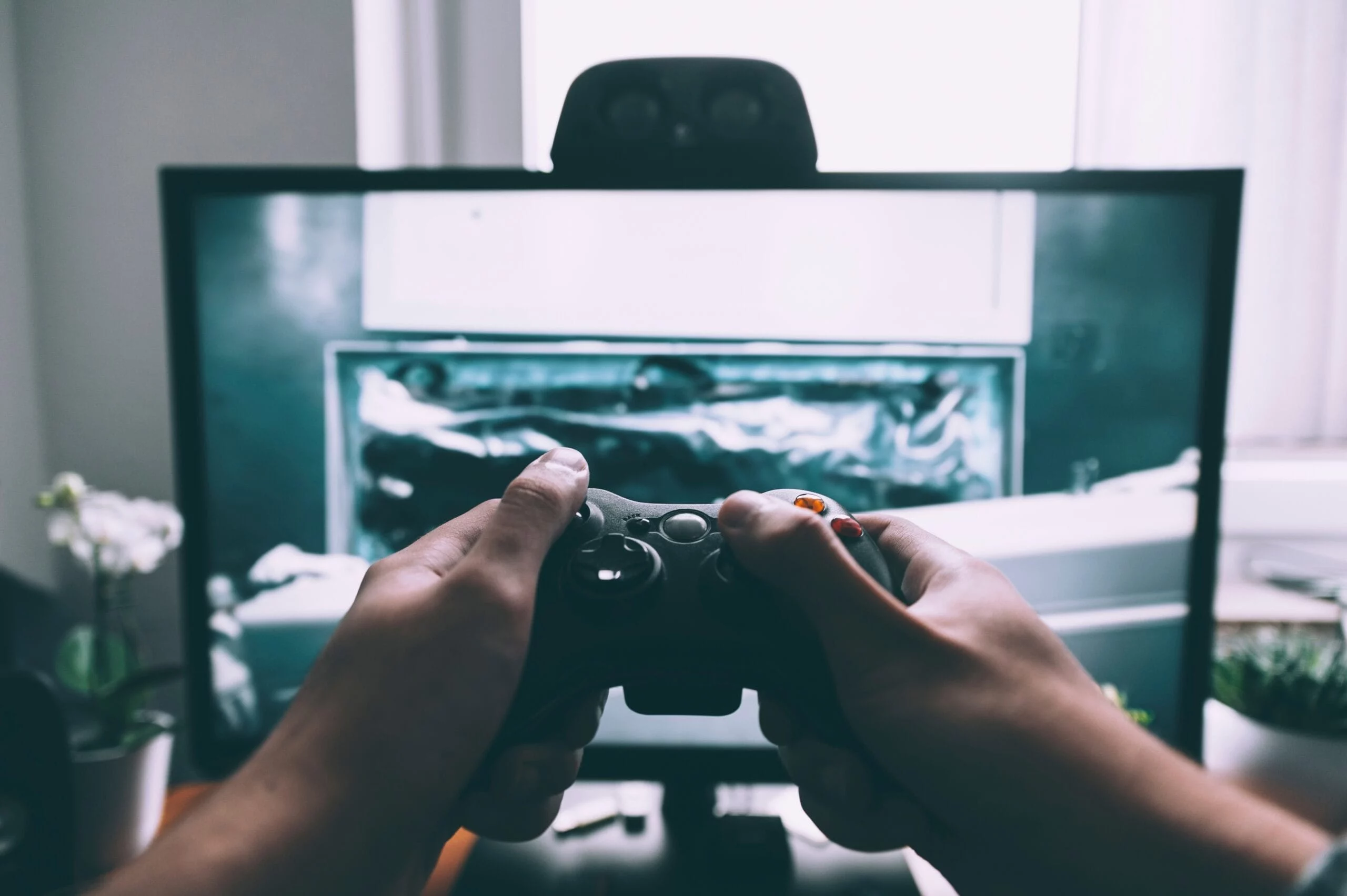 Hände mit einem Gamecontroller vor einem Bildschirm